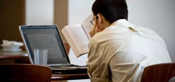 Distance Learning. Student reading a book and looking at a laptop