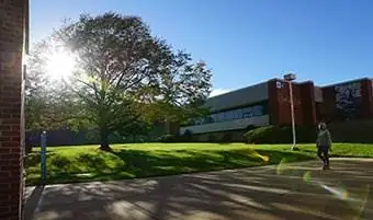 Sun shining on campus with a student walking by a building