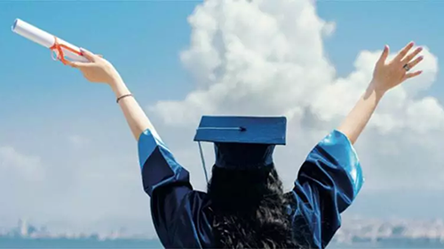 College graduate with hands upstretched to clouds.