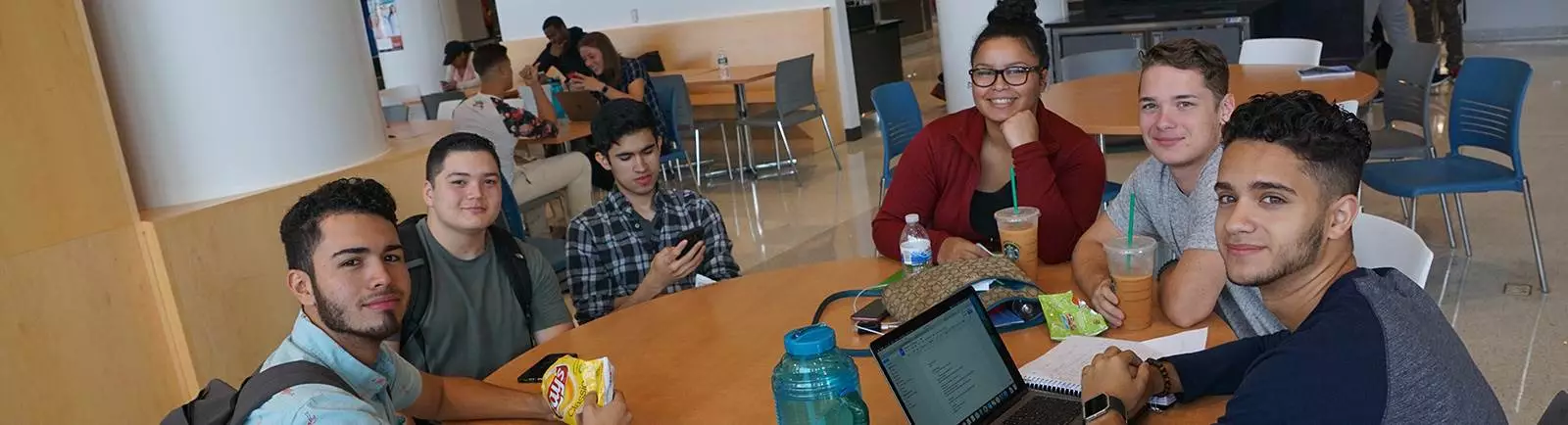 A group of students sitting at a table working and smiling at the camera.