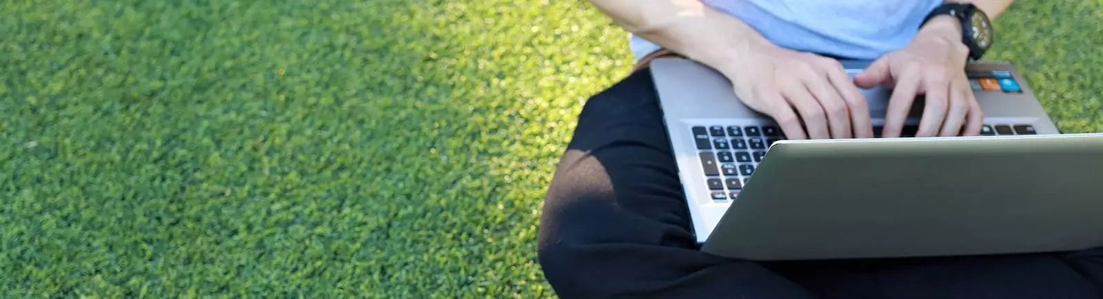 person sitting on grass typing on a laptop