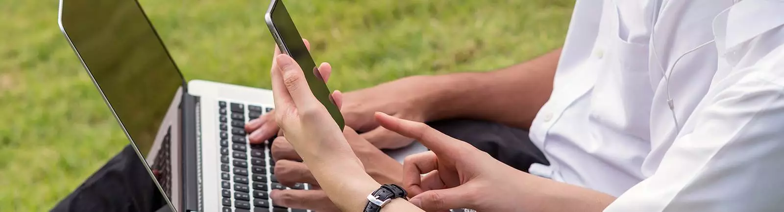 close up on two sets of hands, one holding a phone and one holding a laptop