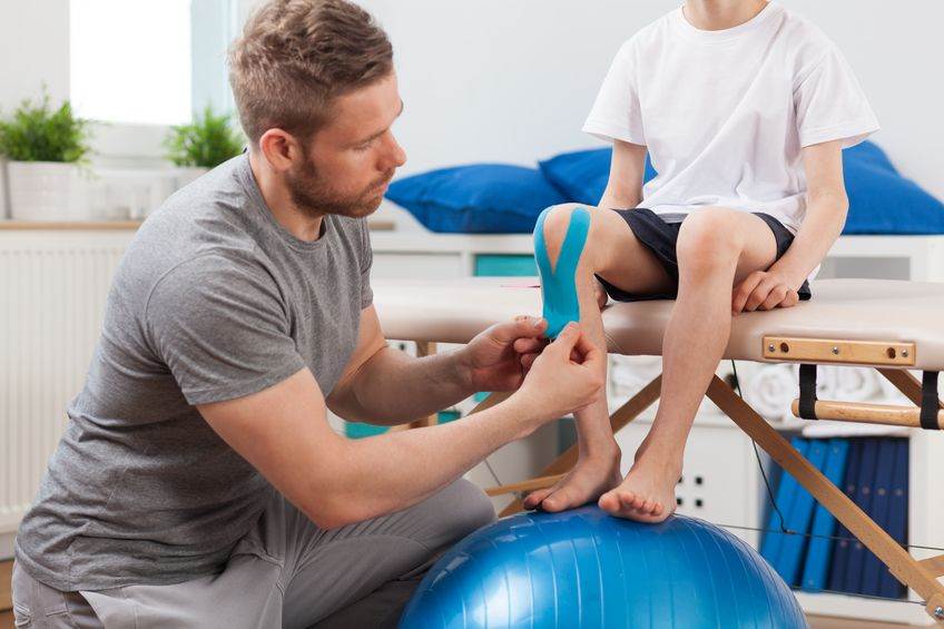 Physical therapist putting KT tape on a child's knee.