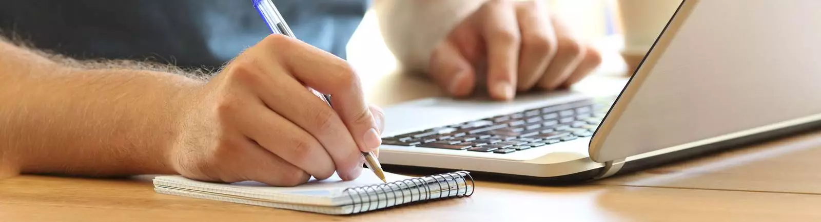 close up of hands taking notes on a note pad from a laptop