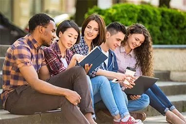 group of students sitting with books and a laptop on a college campus