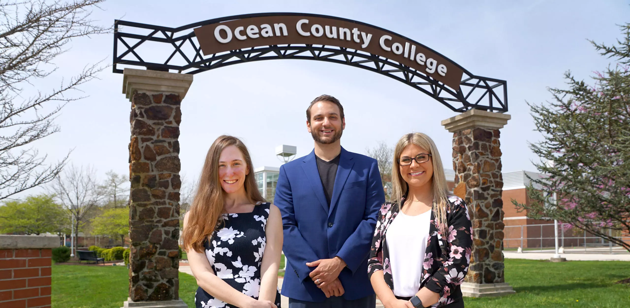 alumni Laura Wagner, Joe Mercadante, and Lisa Wit standing in from of the Ocean County College archway