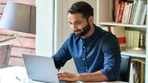 Man sitting at a desk on his laptop in front of a bookshelf