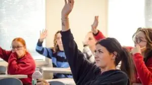 Student in front of room raising hand to ask a question