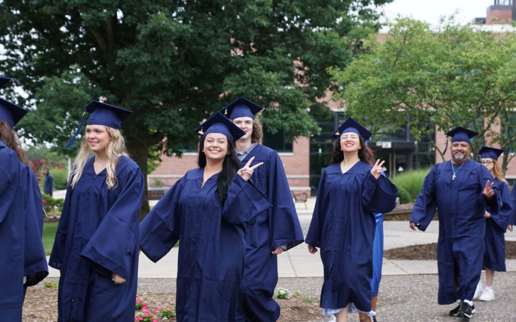 Students at graduation smiling at the camera and showing peace signs with their hands.