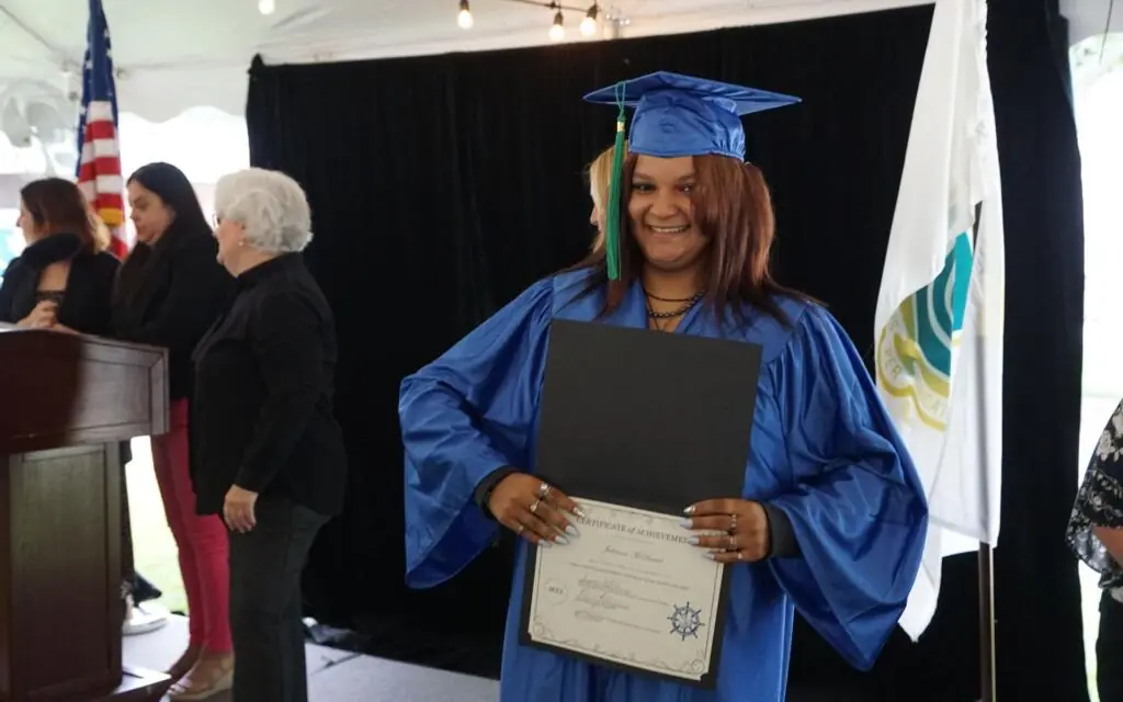 Smiling woman proudly showing her diploma in her graduation cap and gown