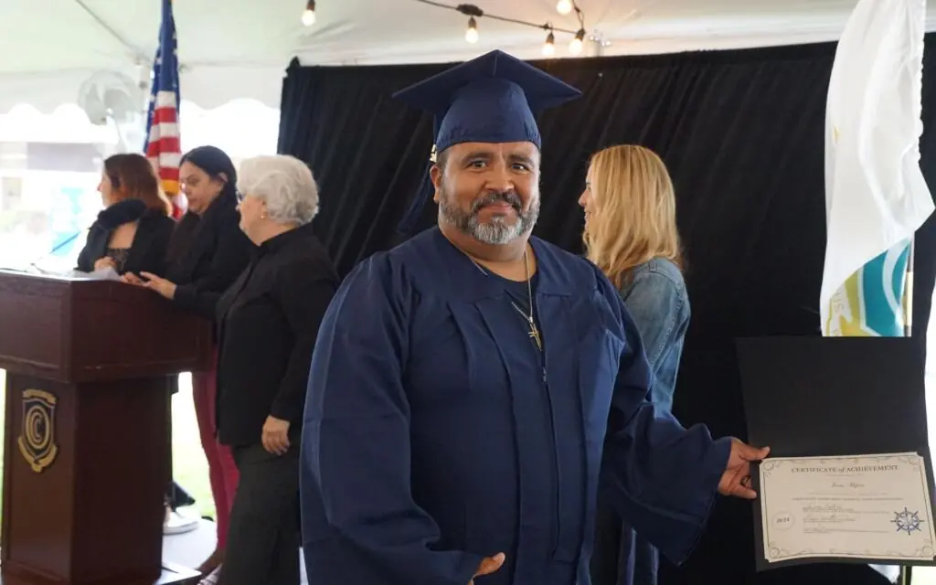 Man with a greying beard in a graduation cap and gown