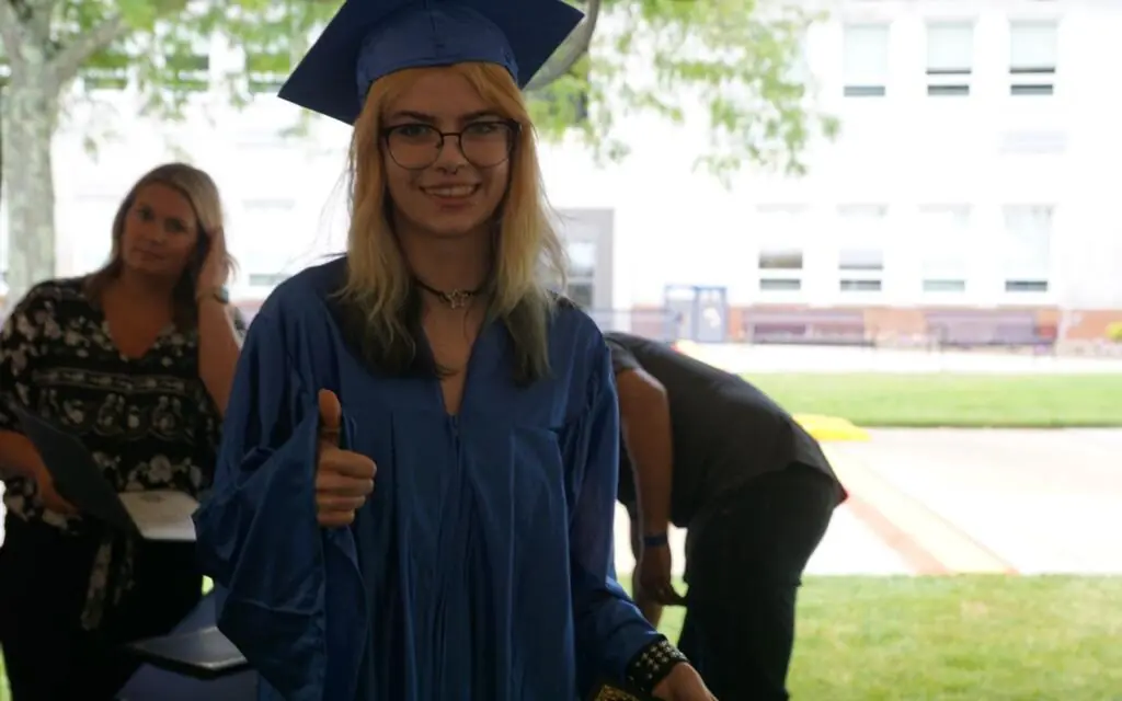 woman with glasses in a graduation cap and gown giving a thumbs up