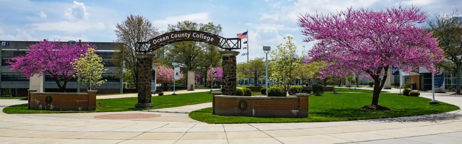 Campus photo of the Ocean County College arch with flowering trees in spring