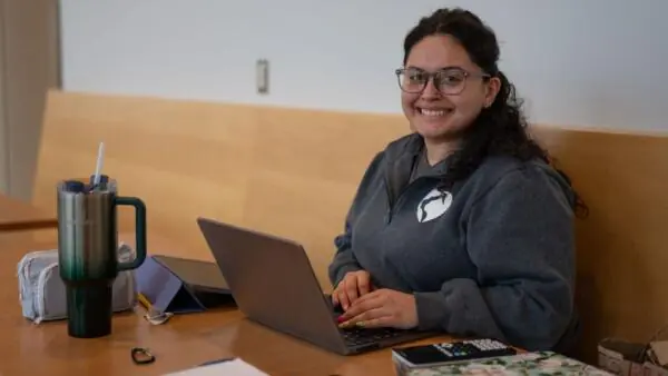 Female student working on her laptop smiling at the camera.