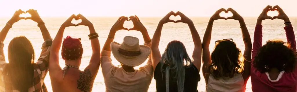 Photo of a group of women facing away from the camera with their hands raised above their heads making a heart with their hands