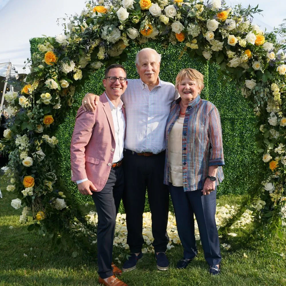 Three people smiling in front of a flower sculpture 