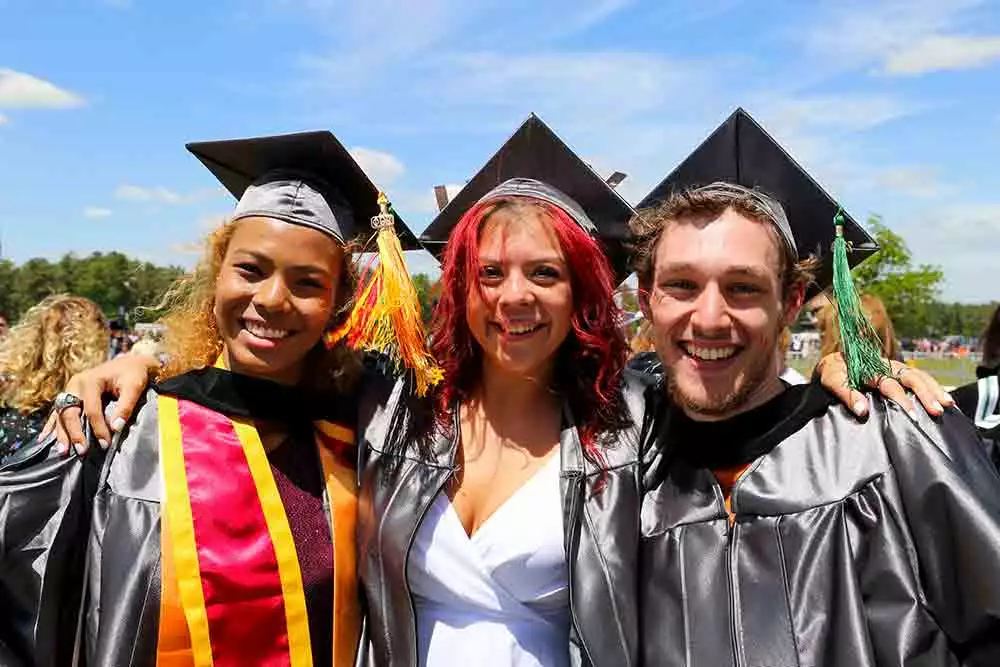 Three students smiling dressed in graduation caps and gowns.