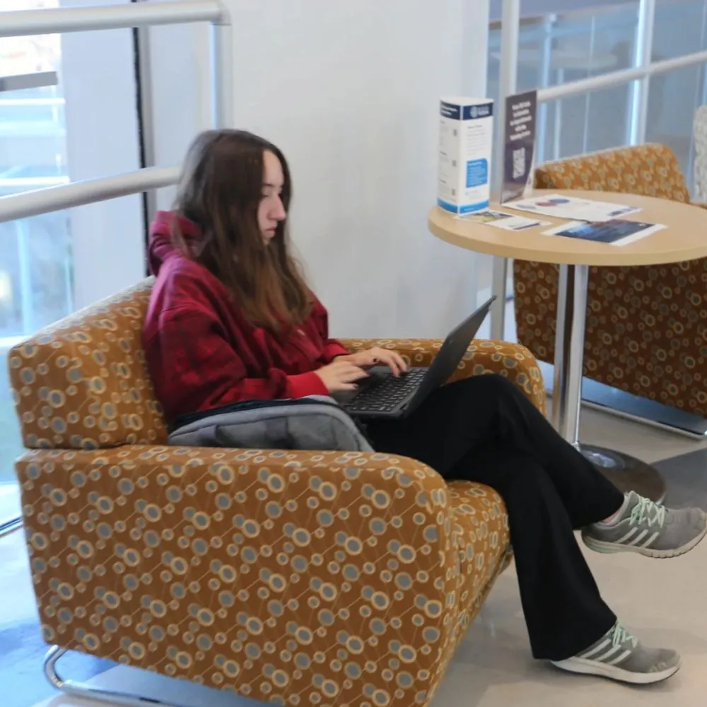 Girl working on a laptop while sitting in a chair on campus