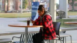 Student texting on campus while drinking coffee.