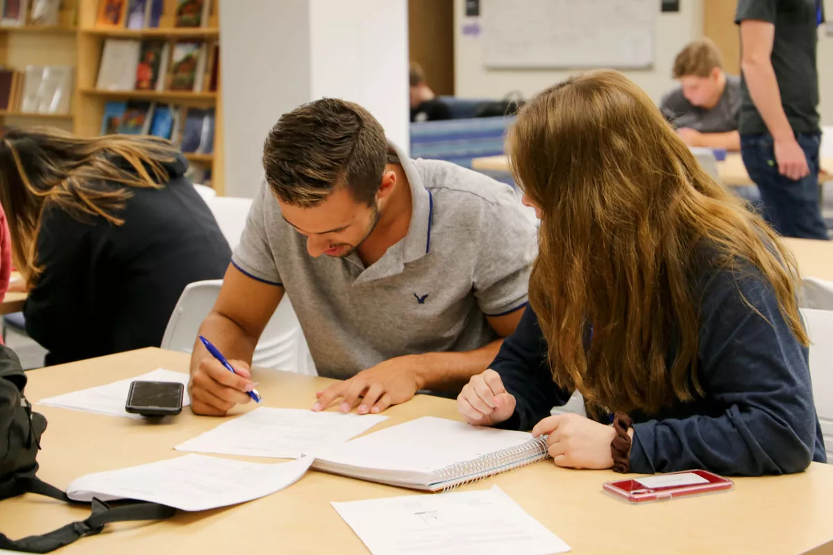 A female student tutoring a male student in a library.