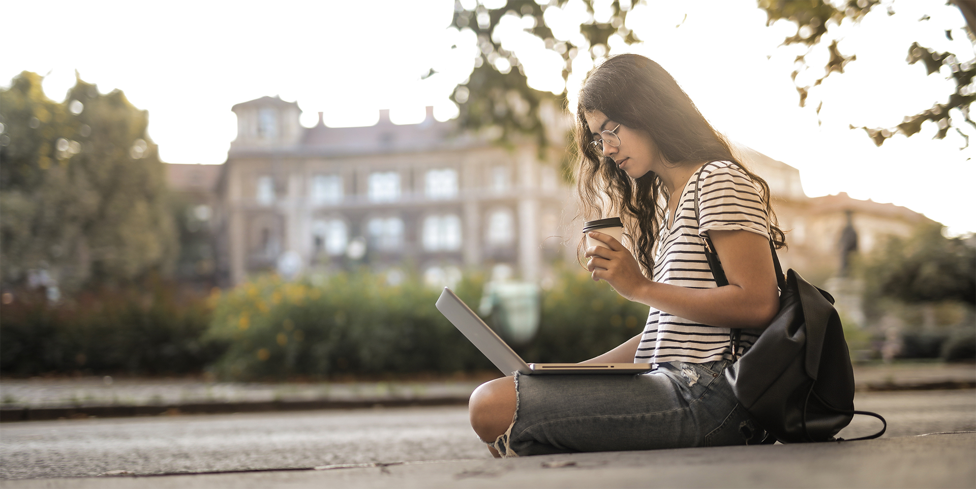 Woman sitting on the ground using a laptop on campus.